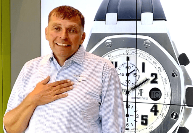 Andreas Hildebrand vor einer überdimensionalen Audemars Piguet Uhr mit dem Hinweis auf ein Willkommens Video