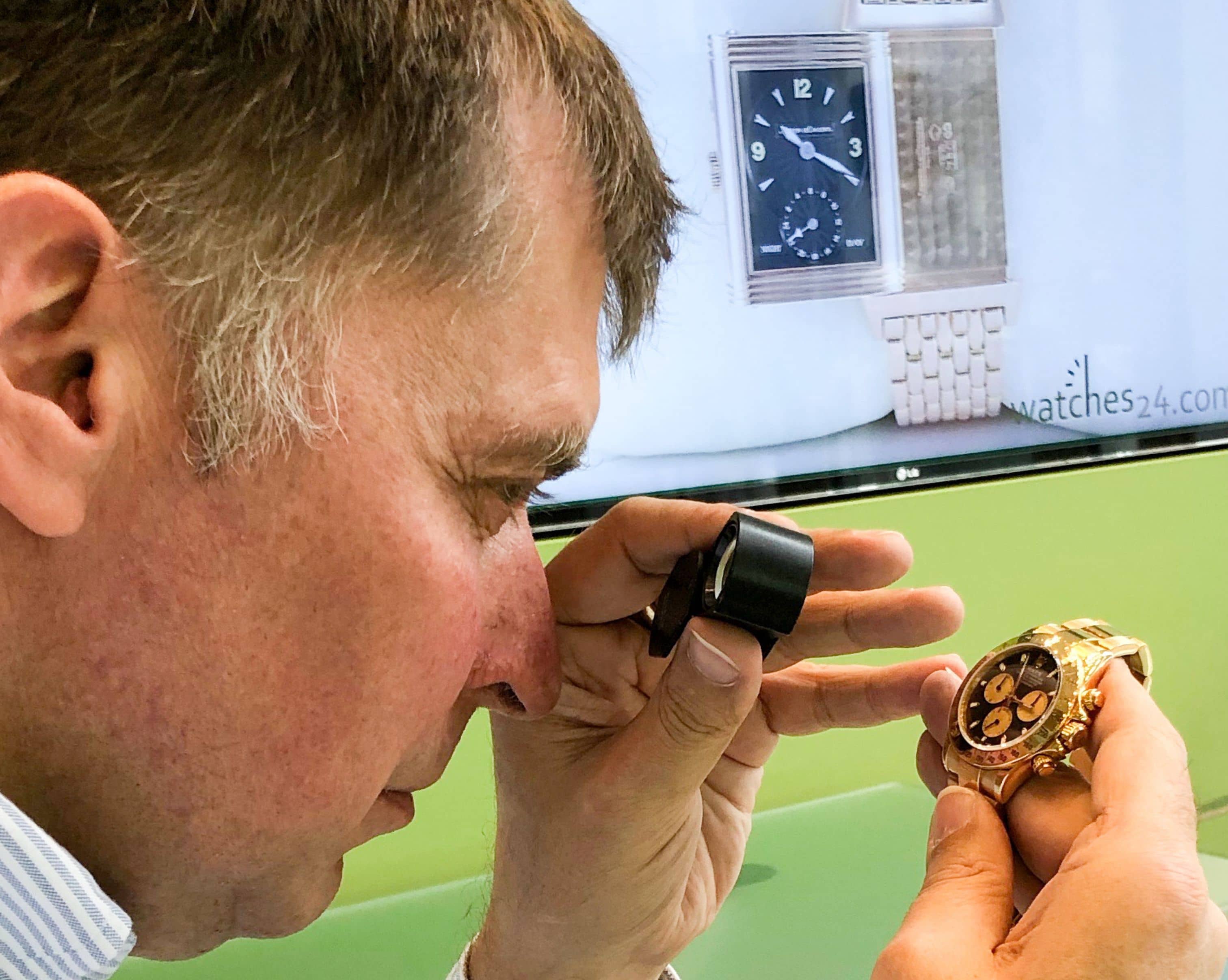 Inhaber Andreas mit Lupe vor einer Uhr im Hintergrund eine Uhr auf dem Monitor